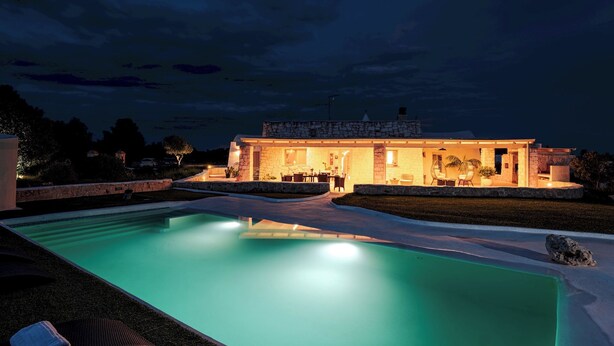 Une maison moderne dotée d’une piscine, d’une façade en pierre et d’un espace extérieur aménagé pour se détendre.