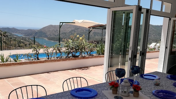 Comedor con una mesa lista para cuatro, con vista a una piscina y montañas.