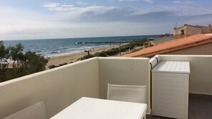 Un balcón con una mesa y una silla blancos, con vista a una playa y al mar.