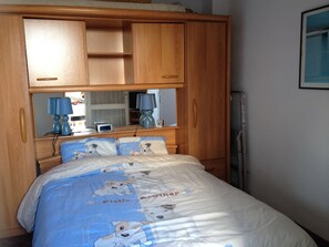 A bedroom with a bed, wooden wardrobe, bedside lamps, and a mirror.