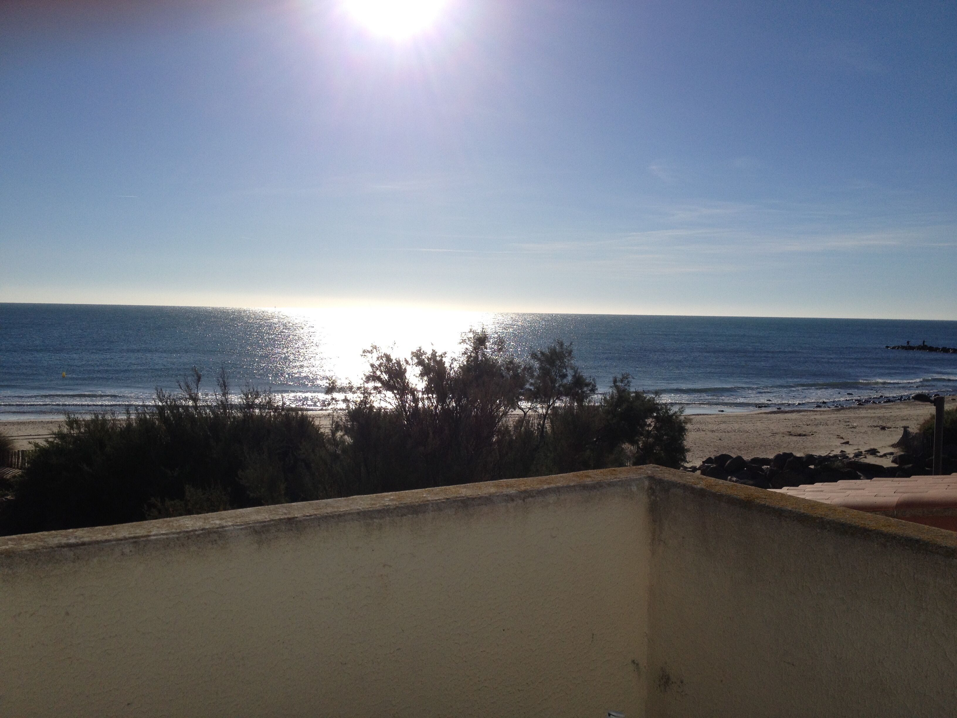 A beach view from a balcony with a clear sky and the sun shining.