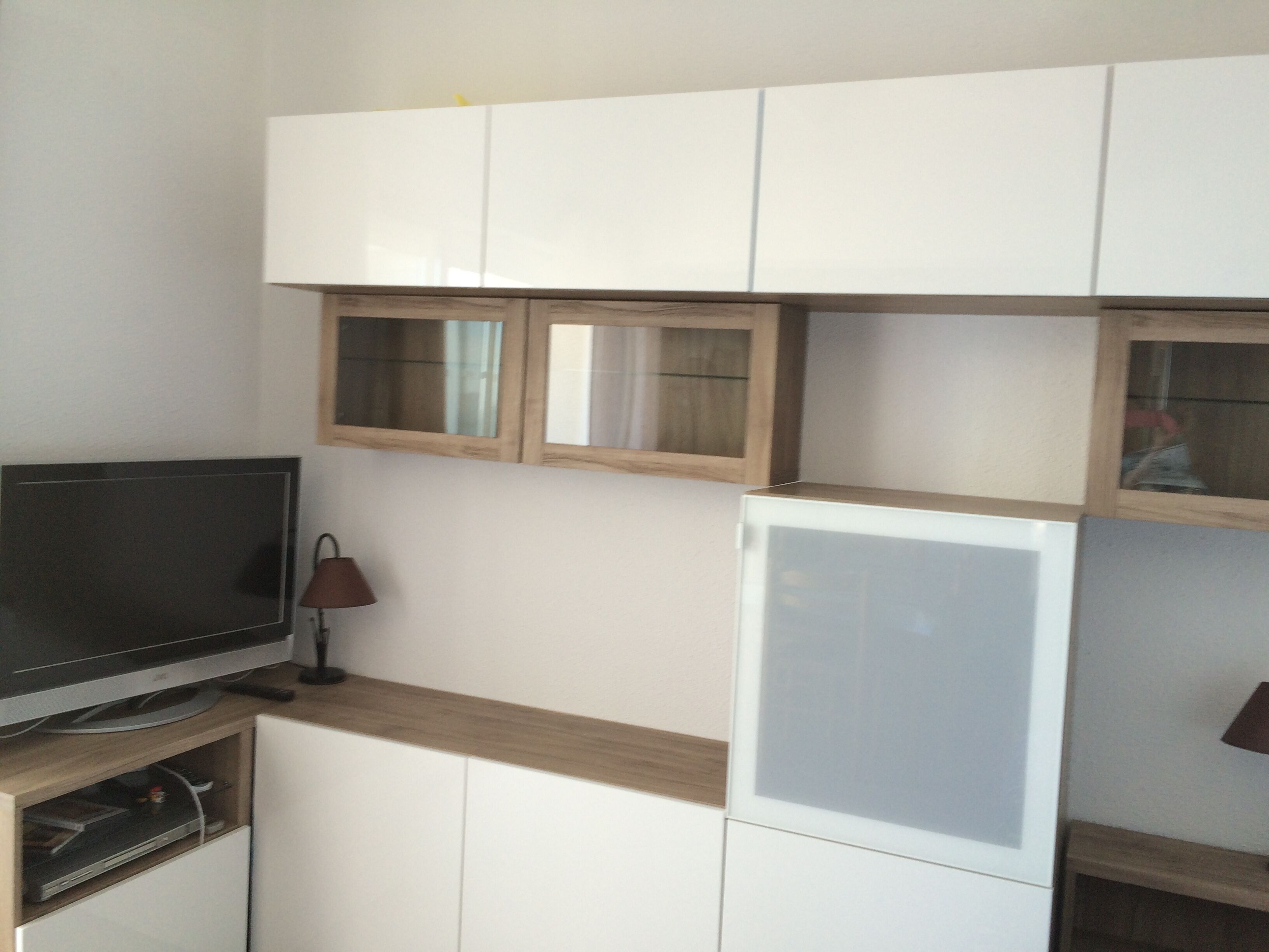 Una cocina compacta con armarios blancos, televisor integrado y refrigerador.