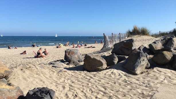 Una playa arenosa con rocas grandes y una valla de madera.