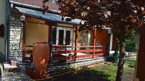 A stone building with a wooden porch, a large urn, and a hose on the ground.
