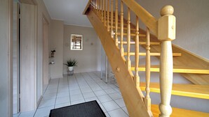 Un escalier en bois, doté d’une rampe, mène à l’étage supérieur. Une plante en pot se trouve sur le palier.