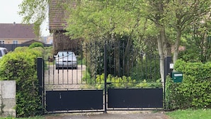 Un vialetto recintato che conduce a una zona residenziale, con un'auto parcheggiata e una casa sullo sfondo.