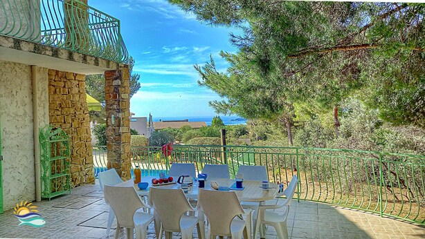 Une terrasse avec une table et des chaises, offrant une vue panoramique sur la mer et les arbres.