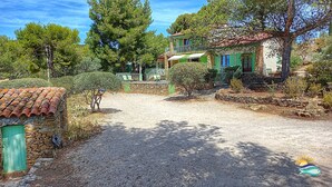 Une maison de campagne en pierre, avec une allée en gravier, entourée d’arbres et d’un petit jardin.