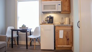 Une cuisine compacte avec des meubles en bois, un réfrigérateur blanc, un four à micro-ondes et une machine à café. On y trouve un petit coin repas avec deux chaises blanches et une table.