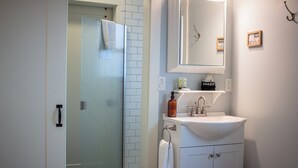 Une salle de bain avec une porte de douche en verre, un lavabo blanc avec un miroir au-dessus, et une serviette suspendue à un porte-serviettes.