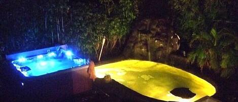 A hot tub and a sunken seating area at night, surrounded by trees and a rock formation.