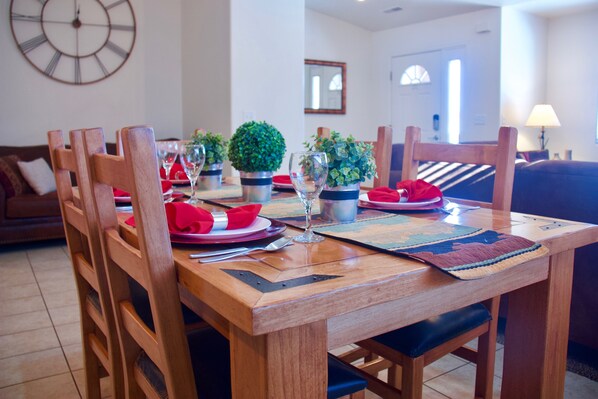 Una mesa de comedor dispuesta con servilletas rojas, platos y vasos, rodeada de sillas de madera.