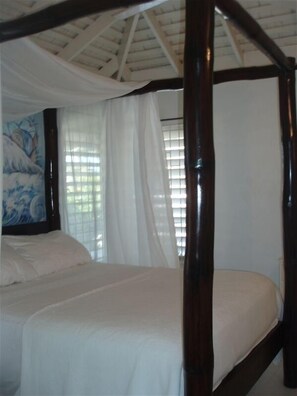A single bed with a wooden frame in a room with a sloped ceiling and a large window with white curtains. - ONE RHYTHM VILLA - Steps to the BEACH - CHEF Included - Caribbean Sea Views (duncans bay)