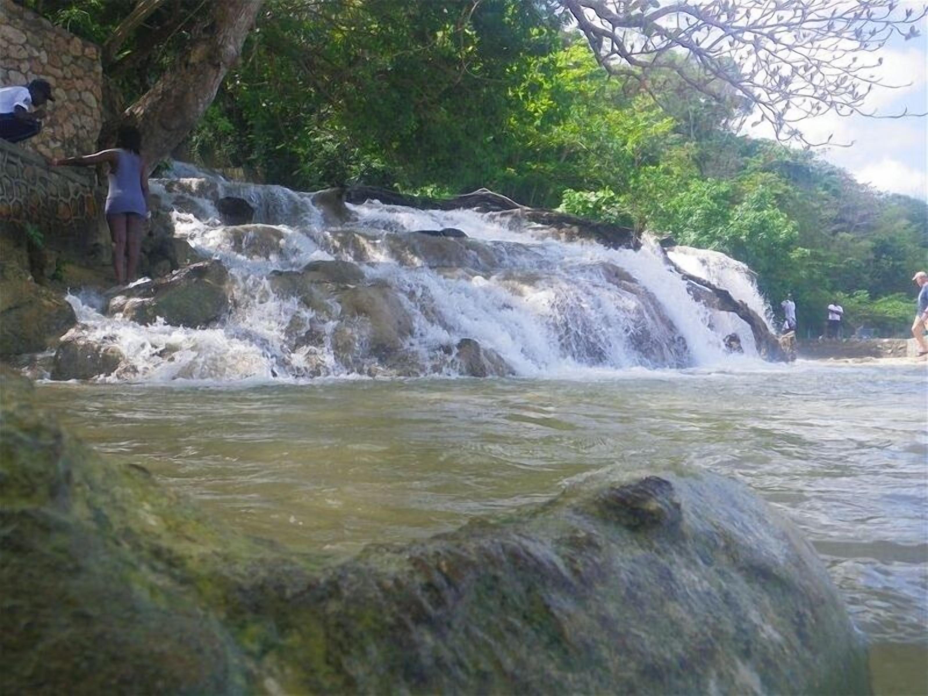 A waterfall with a stone wall and a large rock in the foreground.