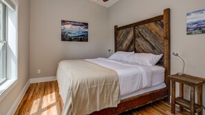 A bedroom with a wooden headboard, a bed with white linens, a ceiling fan, and two wall-mounted paintings.