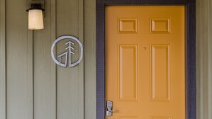 A wooden door with a metal handle and a peephole, a light fixture above it, and a circular sign with a tree symbol.