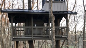 Ein Baumhaus mit einem Balkon, umgeben von Bäumen in einem Wald.