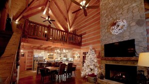 Ein geräumiges Wohnzimmer mit hoher Decke, Holzbalken, einem Kamin und einem Weihnachtsbaum.