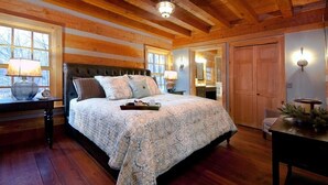 Ein Schlafzimmer mit einem großen Bett, Holzwänden, Holzboden und einem Fenster mit einer Lampe auf dem Nachttisch.