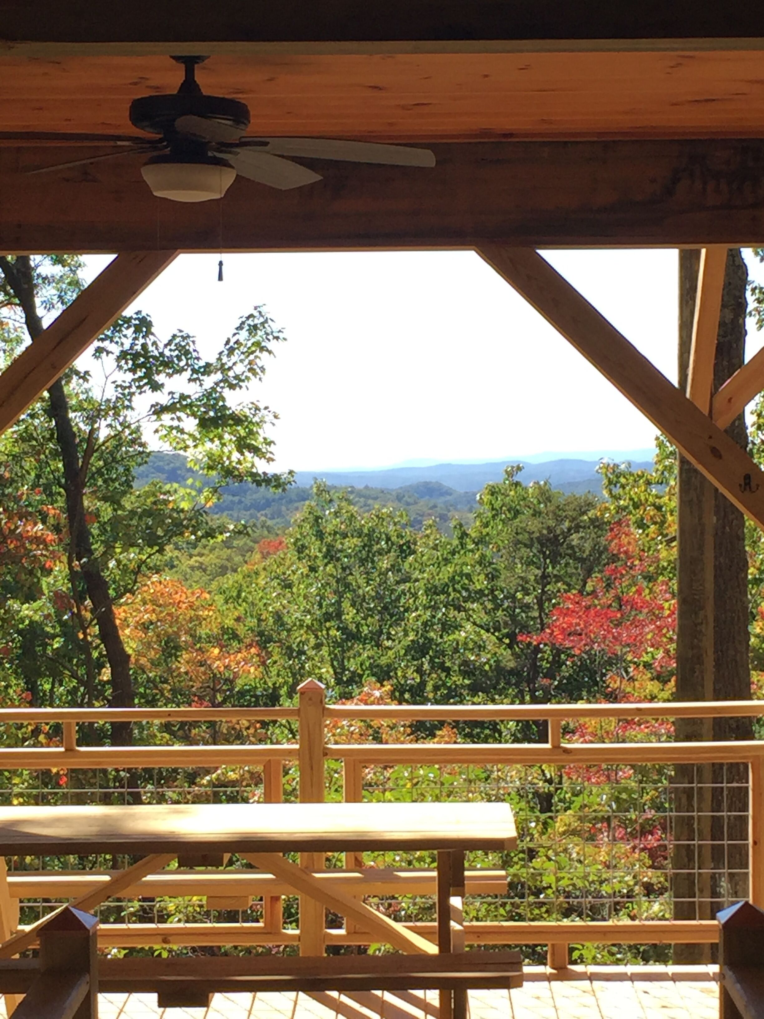 Eine Holzterrasse mit Tisch und Stühlen, mit Blick auf eine bewaldete Landschaft und entfernte Berge.