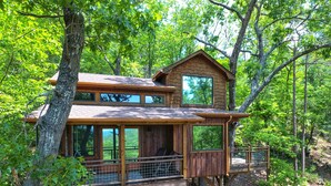A wooden treehouse with multiple levels, large windows, and a balcony. - Canopy Blue Luxury Treehouse *hot tub, fire pit, swing bed, amazing views* (Blue Ridge)