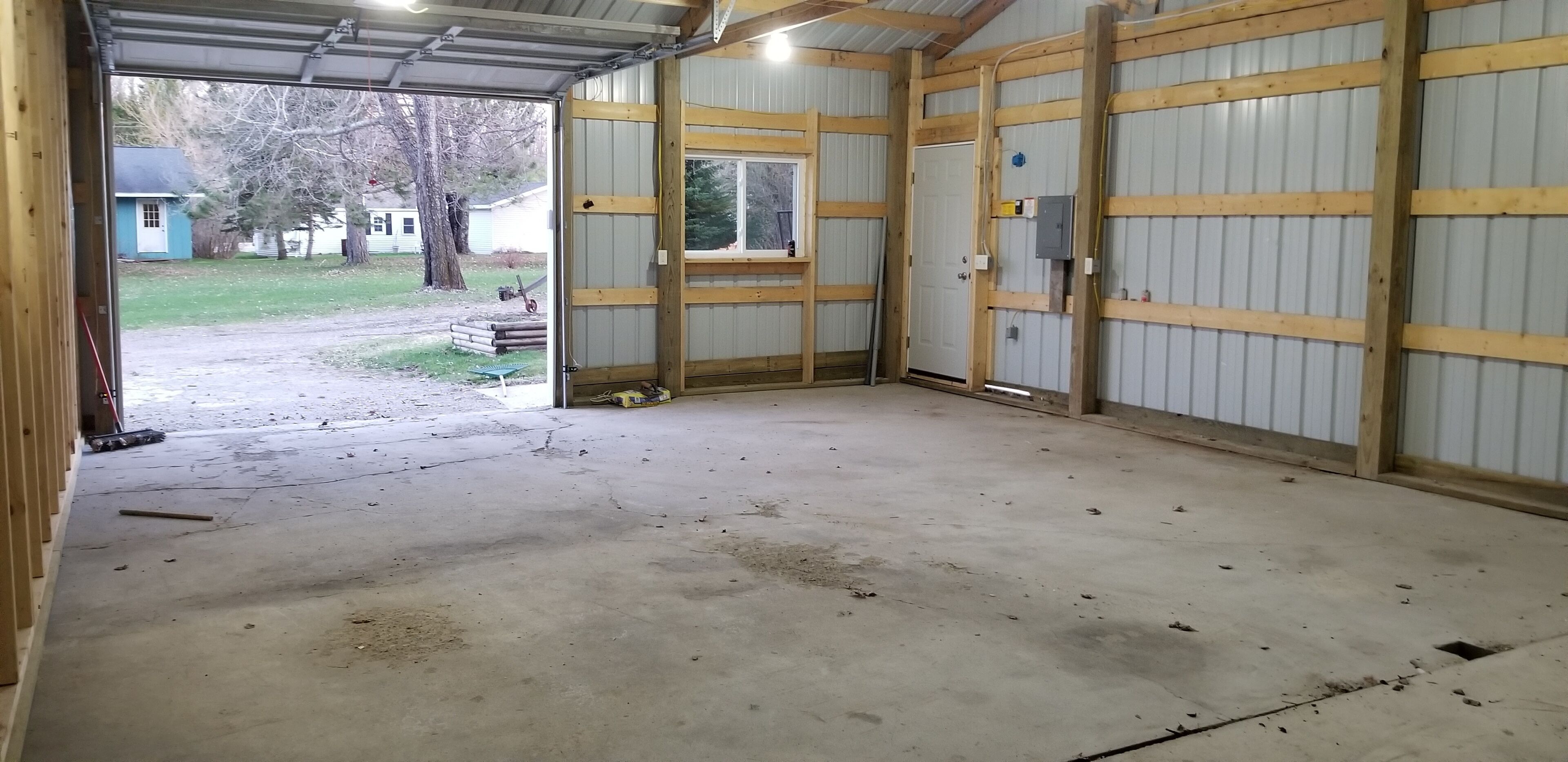 Eine geräumige, offene Garage mit Betonboden, Holzbalken und einer Metalttür.