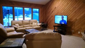 A living room with a beige sofa, a coffee table, and a television on a wooden wall.