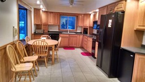 A kitchen with wooden cabinets, a black refrigerator, a dining table with chairs, and a window with a view.