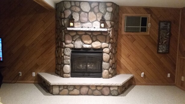 A stone fireplace with a mantel, flanked by wooden walls and a wooden floor.