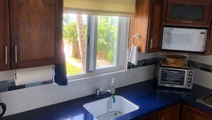 A kitchen with wooden cabinets, a microwave, a toaster, and a window with a view of greenery. - BEACHFRONT on a Budget! ~ Condo Sereno ~ Low Beachfront Rate! (BUCERIAS)
