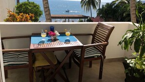 A wooden table with two chairs, a blue placemat, and a glass of orange juice. - BEACHFRONT on a Budget! ~ Condo Sereno ~ Low Beachfront Rate! (BUCERIAS)