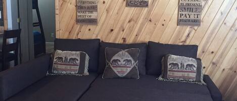 Un canapé de couleur sombre, agrémenté de trois coussins décoratifs, est placé contre un mur en bois où sont inscrites des citations inspirantes.