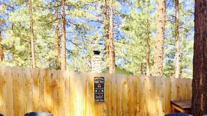 A fire pit area with two Adirondack chairs and a wooden fence in a forested setting.