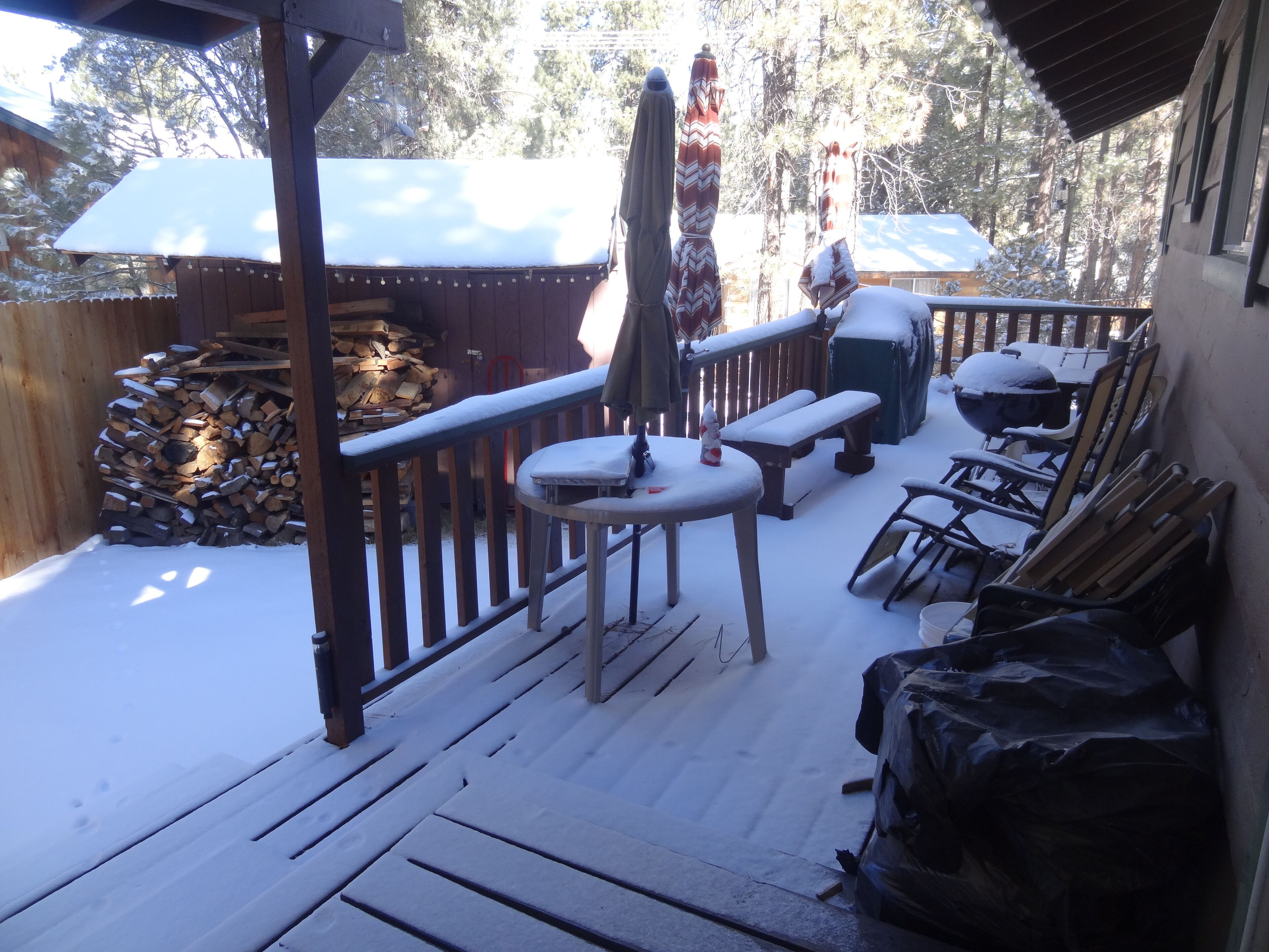 A wooden deck with a snow-covered patio area, including a table, benches, and outdoor furniture.