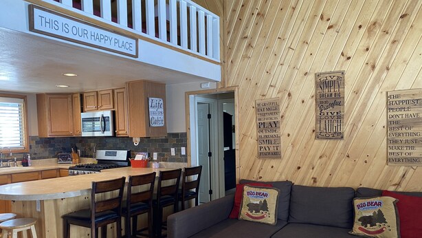 A cozy cabin interior with a kitchen, dining area, and a living room with a couch and pillows.