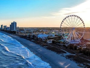 A coastal cityscape with a prominent Ferris wheel, beachfront, and modern buildings.