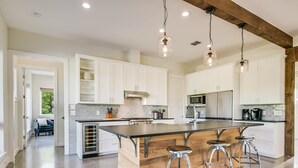 Una cocina amplia con una isla grande, armarios blancos y electrodomésticos modernos.