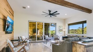 Una sala de estar moderna con chimenea de piedra, ventilador de techo y un televisor grande en la pared.