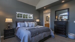 Une chambre à coucher comprenant un lit, des tables de chevet, une commode, un miroir et une fenêtre.