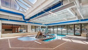 Una piscina interior con tobogán, ventanas amplias y un techo alto con tragaluces.