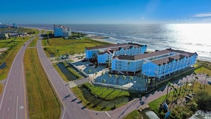 A coastal hotel with a large parking lot, a road curving around the property, and a view of the ocean.