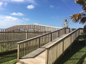 A wooden boardwalk with a spiral staircase leading to a viewing platform, surrounded by a fence and palm trees.