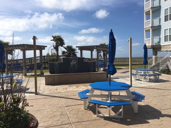 A poolside area with blue and white picnic tables, umbrellas, and lounge chairs.