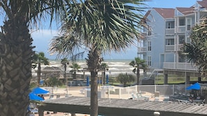 A pool area with lounge chairs and umbrellas, a view of the ocean, and a building with multiple balconies.