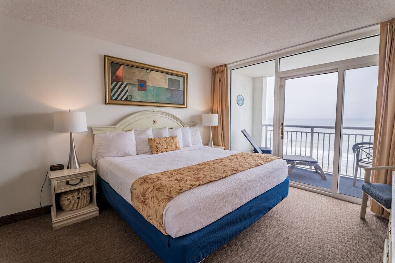 A hotel room with a large bed, a balcony with a view, and a painting on the wall.