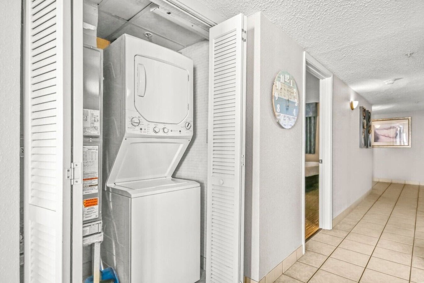 Une buanderie équipée d’un lave-linge et d’un sèche-linge, une horloge au mur et un couloir menant à une autre pièce.