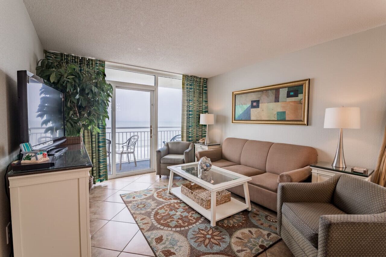 Un salon avec un canapé, une table basse, un téléviseur et un balcon offrant une vue agréable.