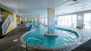An indoor swimming pool with a blue slide, a staircase, and a view of the outside through large windows. - Direct Oceanfront 3BR/2BA, Park on same level as condo (Myrtle Beach)