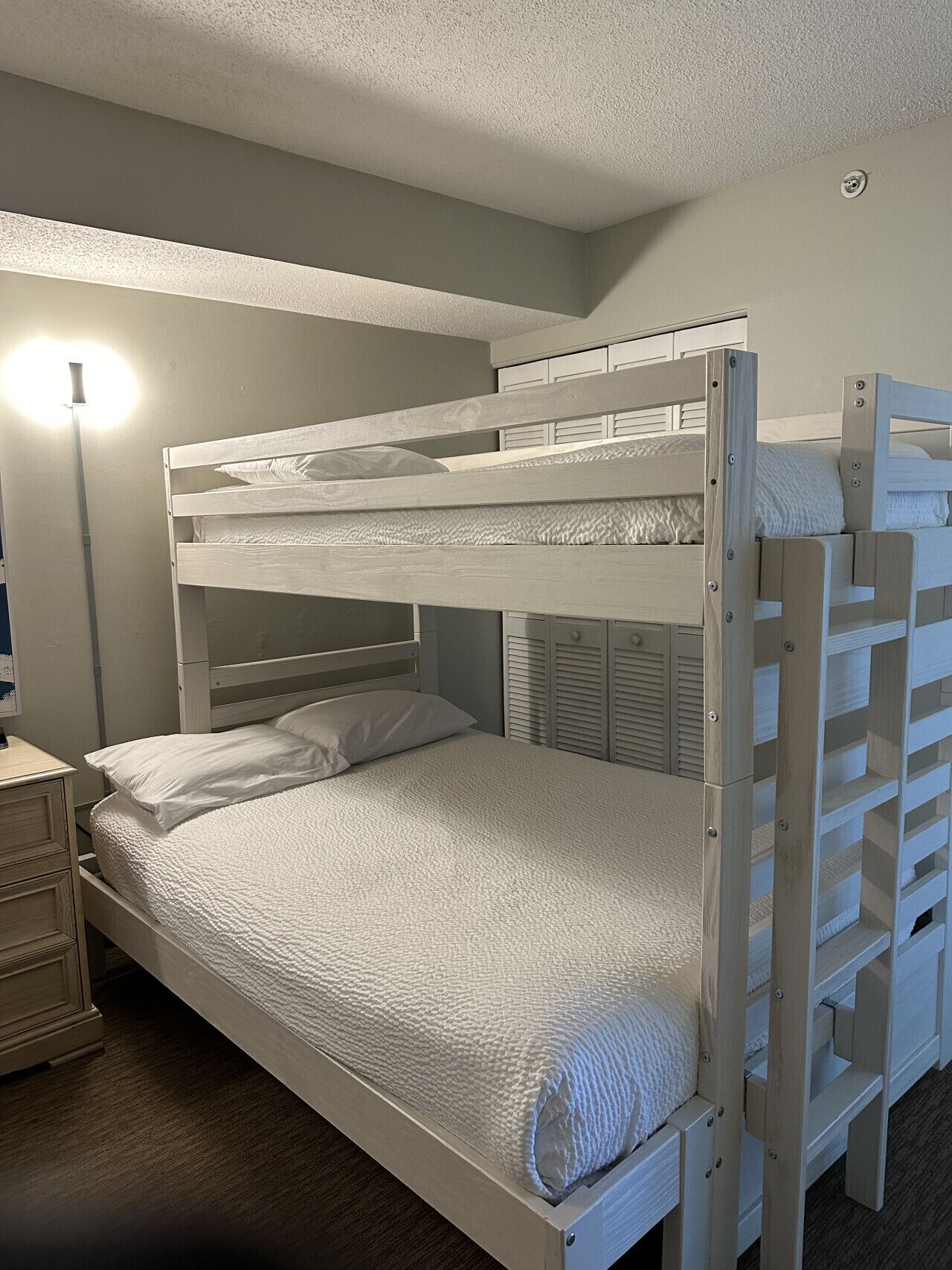 A bunk bed in a room with a bedside table and a lamp.
