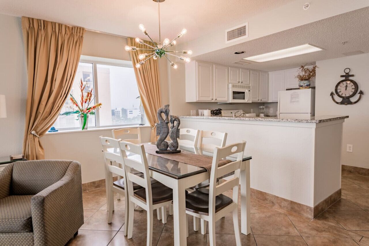 A modern kitchen with white cabinets, a central island, and a dining area with white chairs.
